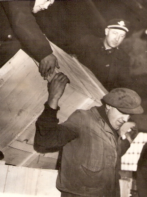  Traja muži, jeden z nich v pracovnom, ost. v rovnošate pri prenášaní dreven. debny v interiéri skladu. Text: Žst. Bratislava hl. st. Anon., cca 1960. 110 x 148 