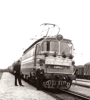  S 489.0087 s tabuľou Splnený záväzok - náš dar k 50. výročiu VOSR a osob. vlakom. Zástup ľudí pri jednom z vozňov. Text: Prvý elektrický vlak v Kútoch. Foto: Andraščík, 1967. 153 x 220 