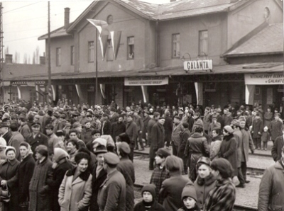  Ozdobená výpravná budova Galanta od koľají, pred ňou dav ľudí. Nápis: Vítame prvý elektrický … v Galante …. Anon, 1969. 180 x 240 