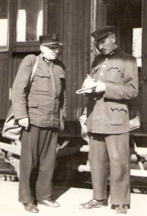  Dvaja muži v železn. rovnošatách (jedna býv. slov., jedna medzivojn. ČSD) so služ. táškami pri dverách služob. vozňa Dd. Anon., cca 1950. 83 x 122 