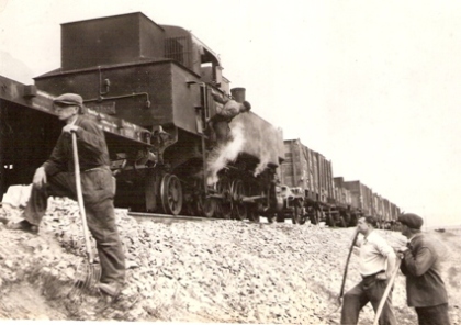  Rušeň 431.024 s prac. vlakom na násype. V popredí robot. s vidlami na štrk. Text: Výstavba Trate Mieru Lučenec - Opatová. Anon., cca 1950. 170 x 120 