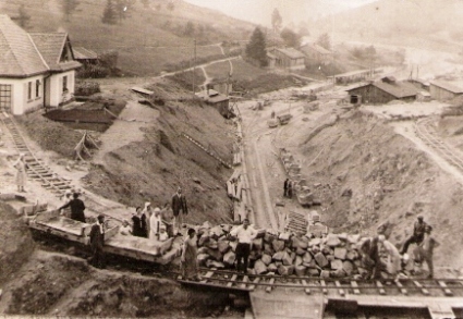  Pohľad z temena tunel. portálu na stav. dvor s diel. budov. a koľaj. prac. drážky s huntíkmi. Vľavo hotový str. dom. Póz. civilisti. Text: Štrajk na výstavbe žel. trate N. Mesto n. V. - Myjava. Anon., cca 1925. 130 x 90 