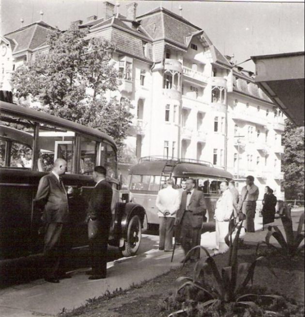  Pohľad zozadu na dva autobusy (predný neurč., zadný Saurer) v Trenčianskych Tepliciach pri liečebnom dome. Vpredu skupinka civilov. Anon., cca 1947. 100 x 100 