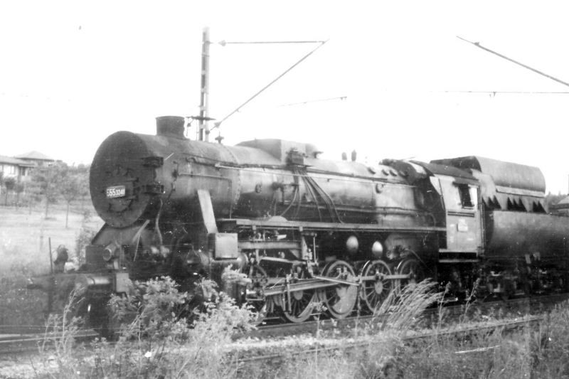  Parný rušeň 555.3240 na dvojkoľajnej elektrifik. trati. Pohľad zľava zpredu. Trakč, podpery, vľavo vzadu obyt. domy. Anon., cca 1970. 177 x 118 