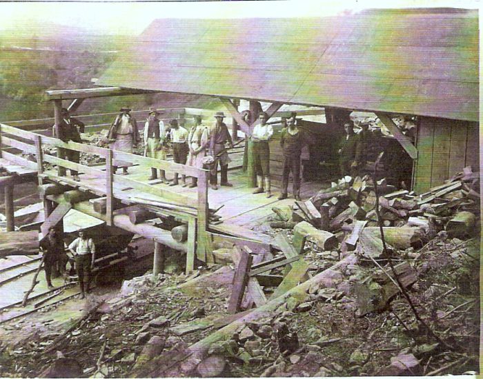  Skupina mužov v civile i krojoch na drevenom, čiast. zastrešenom lešení nad dvoma koľajami pracovnej drážky. Text: Výstavba trate Zvolen - Krupina. Foto: Anon., cca 1923, farebná xerokópia. 112 x 83 