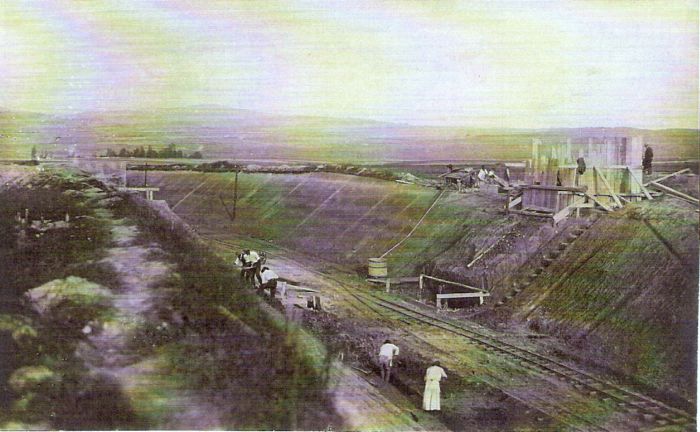 Široký zárez, v ňom pracovná drážka, kaďa na vodu a pracujúci muži v civile a krojoch. Text: Výstavba trate Zvolen - Krupina. Foto: Anon., cca 1923, farebná xerokópia. 140 x 91 