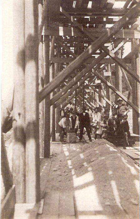  Veľké drevené lešenie. Pohľad v jeho osi. Ľudia v civile a krojoch. Text: Výstavba trate Zvolen - Krupina. Foto: Anon., cca 1923, farebná xerokópia. 88 x 141 