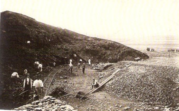  Odkopaný svah, na úpätí stavebná drážka. Ľudia s náradím, vzadu drevené huntíky. Text: Výstavba trate Zvolen - Krupina. Foto: Anon., cca 1923, farebná xerokópia. 145 x 92 