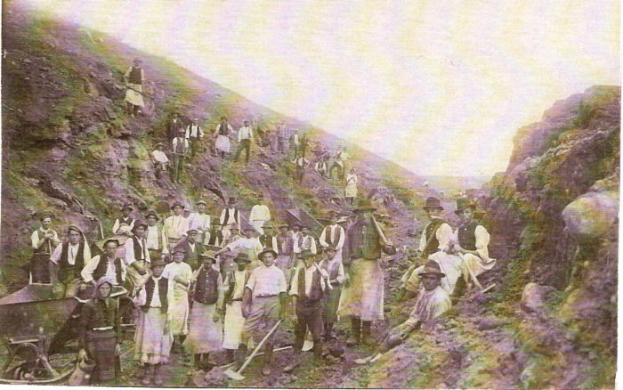  Skupina ľudí v civile a krojoch s náradím v hlinito-skalnom záreze. Pracovná drážka. Text: Výstavba trate Zvolen - Krupina. Foto: Anon., cca 1923, farebná xerokópia. 142 x 90 