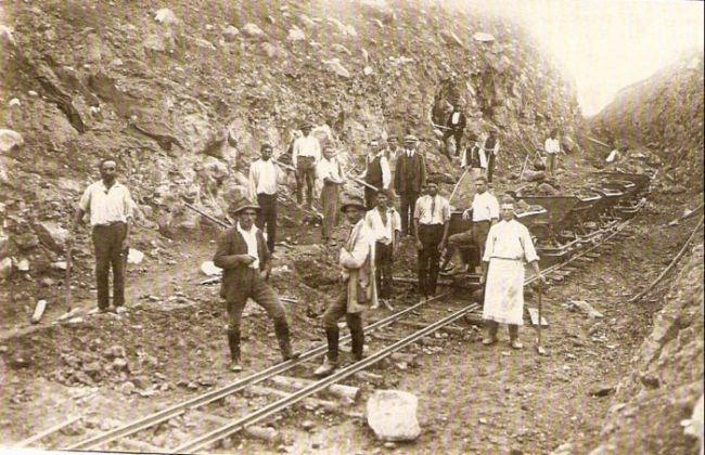  Hlinito-skalný zárez s poľnou drážkou a plech. huntíkmi. Pri drážke robotníci v civile. Text: Výstavba trate Zvolen - Krupina. Foto: Anon., cca 1923, farebná xerokópia. 142 x 93 