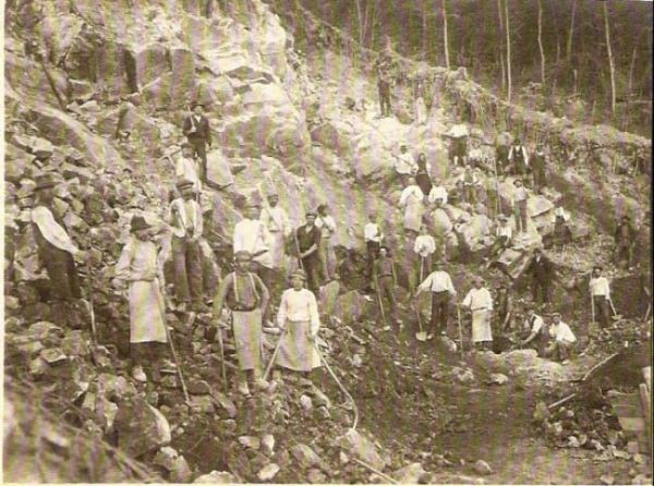  Skalnatý zráz, pózujúci ľudia v civile i pracovnom s náradím. Vzadu stromy. Text: Výstavba trate Zvolen - Krupina. Foto: Anon., cca 1923, farebná xerokópia. 112 x 83 