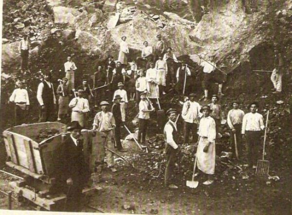  Skalnatý svah. Ľudia s ručným náradím pre zemné práce, vľavo drevený huntík na pracovnej drážke. Text: Výstavba trate Zvolen - Krupina. Foto: Anon., cca 1923, farebná xerokópia. 110 x 82 
