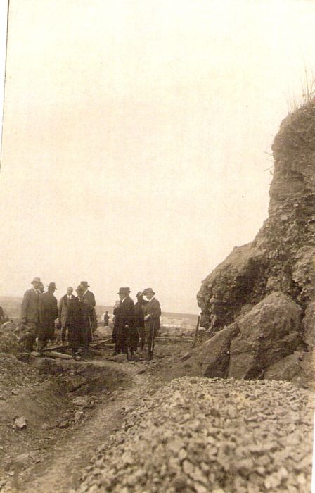  Skupina ľudí v sviatočnom civile (komisia ?) při sklanom svahu. Vzadu budovy. Text: Výstavba trate Zvolen - Krupina. Foto: Anon., cca 1923, farebná xerokópia. 89 x 138 