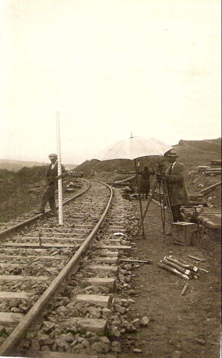  Železničná trať v ľavom oblúku. Vpredu zememerač s theodolitom pod slnenčníkom a figurant s trasírkou. Text: Výstavba trate Zvolen - Krupina. Foto: Anon., cca 1923, farebná xerokópia. 90 x 142 