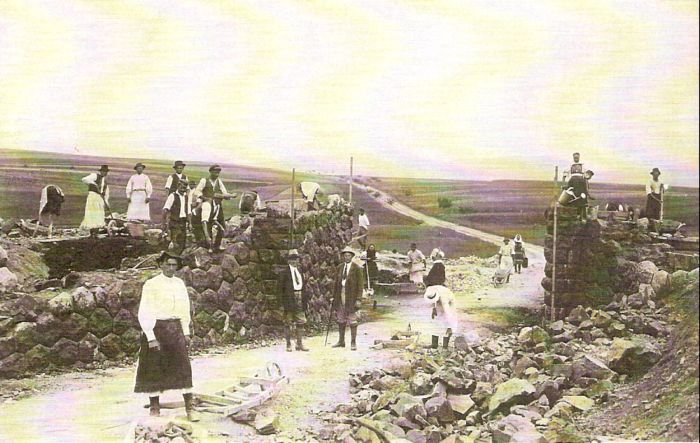  Kamenný nadjazd železnice nad cestou v stavbe. Práce na oporách. Ľudia v krojoch a civile s drev. fúrikmi, dvaja úradníci v civile. Pohľad do krajiny, vzadu hory. Text: Výstavba trate Zvolen - Krupina. Foto: Anon., cca 1923, farebná xerokópia. 143 x 90 