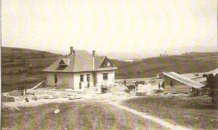  Rozostavaná malá výpravná budova, okolo prac. drážka, plech. huntík. Ľudia pri práci. Vpravo prístrešok, vzadu horská krajina a kostolík. Text: Výstavba trate Zvolen - Krupina. Foto: Anon., cca 1923, farebná xerokópia. 143 x 90 