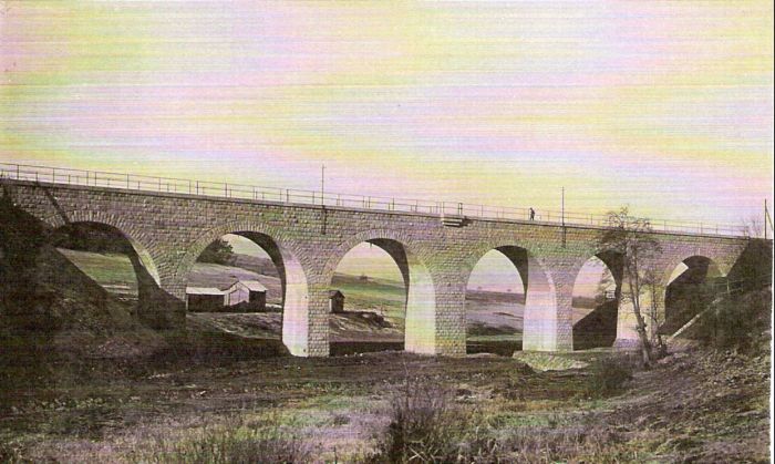  Kamenný železničný most. Pohľad zboku. Vzadu zvažujúca sa krajina, pri moste drevené prístrešky. Text: Výstavba trate Zvolen - Krupina. Foto: Anon., cca 1923, farebná xerokópia. 137 x 89 