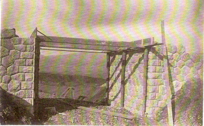  Kamenný železničný mostík v stavbe. Rozpracované opory, drevené paženie. V priehľade mostom horská krajina. Text: Výstavba trate Zvolen - Krupina. Foto: Anon., cca 1923, farebná xerokópia. 139 x 89 