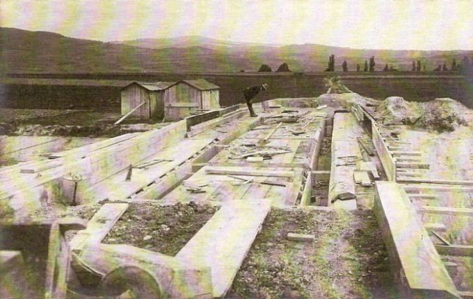  Debnenie pre betónovanie cestného mosta cez trať. Pohľad v osi cesty. Vľavo dva drevené baraky. Vzadu hory. Text: Výstavba trate Zvolen - Krupina. Foto: Anon., cca 1923, farebná xerokópia. 142 x 90 