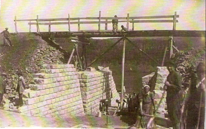  Kamenný železničný mostík v stavbe. Rozpracované opory. Provizórne drevené premostenie. Ľudia pri práci. Text: Výstavba trate Zvolen - Krupina. Foto: Anon., cca 1923, farebná xerokópia. 143 x 92 