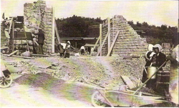  Kamenný železničný mostík počas stavby. Rozpracované opory s dreveným pažením. Ľudia pri práci, drevené fúriky. Vzadu zalesnený kopec. Text: Výstavba trate Zvolen - Krupina. Foto: Anon., cca 1923, farebná xerokópia. 140 x 82 