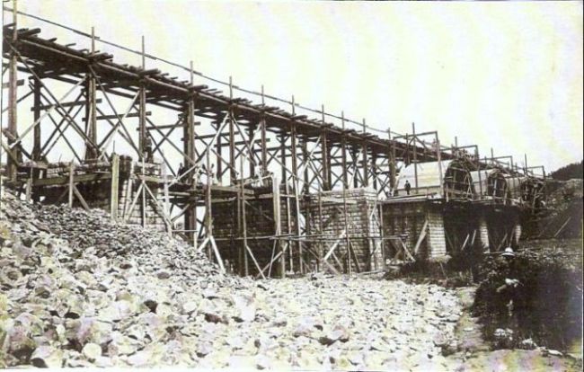  Veľký železničný most v stavbe. Dohotovené piliere, skruže pre klenby, provizórna drevená mostovka, lešenie. Text: Výstavba trate Zvolen - Krupina. Foto: Anon., cca 1923, farebná xerokópia. 143 x 91 