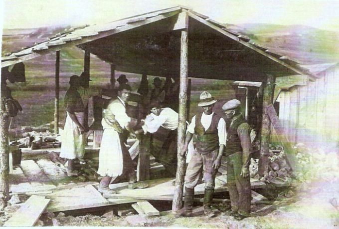  Provizórny prístrešok nad dreveným vrátkom. Obsluhujú ho ľudia v krojoch. Vzadu hornatá krajina. Text: Výstavba trate Zvolen - Krupina. Foto: Anon., cca 1923, farebná xerokópia. 135 x 90 