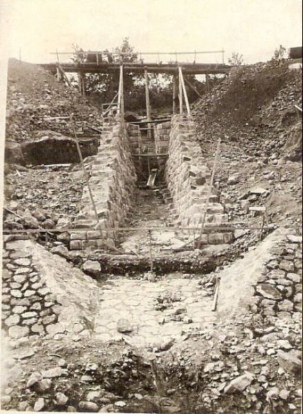  Kamenný priepust v práci. Nad rozpracovaným murárskym dielom provizórne drevené premostenie. Text: Výstavba trate Zvolen - Krupina. Foto: Anon., cca 1923, farebná xerokópia 84 x 114 