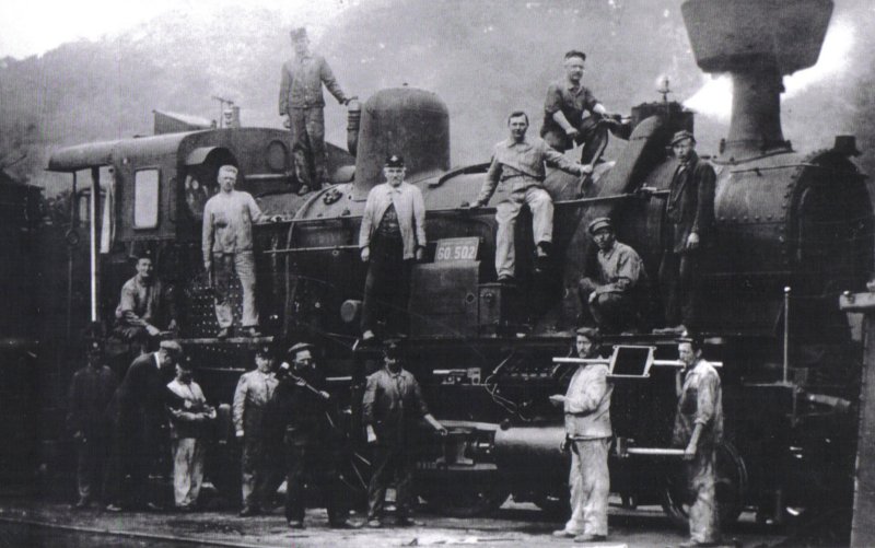  Parný rušeň 60.502 s rozobraným posúvačom. Pohľad zprava zpredu. Pózujúci dielenskí zamestnanci v pracovnom. Foto: Anon., cca 1922, archív Suchý, farebná xerokópia. 243 x 145 