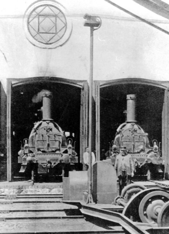  Dva parné rušne triedy I StEG v depe Praha Masarykovo nádr. Čelný pohľad na rušne v remíze. Vpredu presuvňa. Foto: Anon., cca 1900, archív Suchý, fotokópia. 115 x 175 mm 