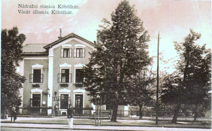  Gbelce (Koeboelkút) - výpravná budova. Čelný pohľad zo strany koľají. Zvonkové návestidlo, petrolejové lampy na konzole i stĺpikoch. Foto: Anon., cca 1920, farebná xerokópia. 273 x 173 