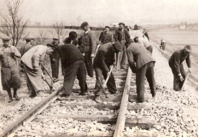  Skupina robotníkov pri ručnom podbíjaní trate. Text: Pracovné brigády železničiarov na stavbe Trate Mieru, Lučenec - Opatová. Anon., cca 1950. 171 x 117 