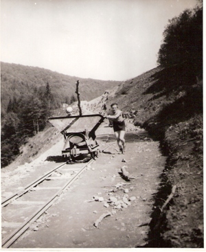  Dvaja mladí robotníci tlačia plech. huntík na prac. drážke v polozáreze - polonásype. Text: Trať Mládeže, výstavba trate. Anon., cca 1950. 142 x 116 