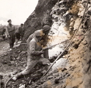  Dvaja vŕtači pri navŕtavaní skalného svahu pneumatickou vŕtačkou. Text: Míneri pri navŕtavaní dier do skál na stavbe Trate Družby. Foto: Kľučka, cca 1955. 125 x 122 