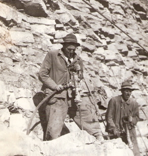  Dvaja muži v pracovnom pri vŕtaní skál pneum. vŕtačkou v skalnej stene. Text: Míneri navŕtavajú diery v kameňolome ČSD Skládaná Skala v výške 110 m na Trati Družby. Foto: Kľučka, cca 1950. 132 x 124 