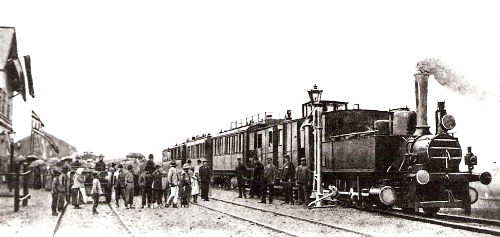  Osobný vlak s 310.4, vodný žeriav, skupina ľudí, mnohí s dáždnikmi. Priečelie vyzdobenej výpr. budovy. Text: Vlak v žst. Bánovce nad Bebravou pri otvorení trate Topoľčany - Trenčín. Anon., 17.8.1901. 125 x 77 