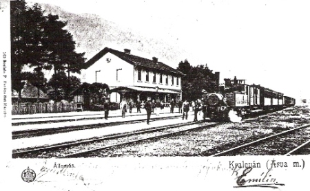  Kraľovany - osobný vlak s 310.4, výpravná budova, koľajisko, pózujúci železničiari i civilisti (xeroxová kópia). Anon., cca 1900. 127 x 70 