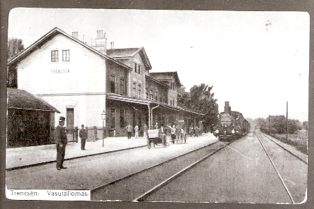  Trenčín - výpravná budova s markízou, koľajisko s vchádz. vlakom, drev. káry na batožinu, železničiari, civilisti. Č-b reprodukcia farebnej pohľadnice. Anon., 1914. 113 x 68, repro: T. Grófová 