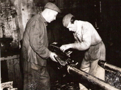  Dvaja muži v pracovnom v dielni pri práci na piestnici s križiakom parného rušňa. Anon., cca 1955. 165 x 124 