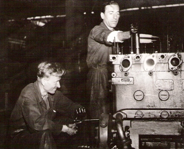  Dvaja muži v prac. pri práci na rozloženom vodou chladenom spaľovacom motore z motorového vozňa. Text: Dielne ČSD Zvolen. Anon., cca 1950. 155 x 125 
