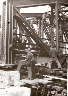  Pohľ. zboku na krajné dve zvislice mosta cez Váh pri Trenčíne. Pole je podopr. pyramíd. z podvalov. Pri a na moste sú ľudia v prac. Text: Trenčín - opr. nem. Vojsk. znič. mosta. Foto: Halaša, J., apr.1945, 90 x 128 