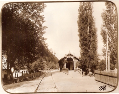  Banská Bystrica-mesto (Szentjános). Jednokoľaj. trať, drev. budova s drev. plotom, telegr. tyče, prechod, petrolej. lampa na drev. stĺpe. Foto: Kóczány, 1896. 225 x 175 