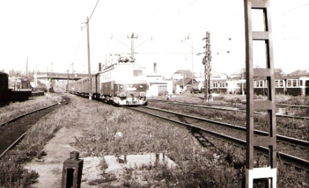  Poprad-Tatry - pohľad na vchádzajúcu raketu s E 499.0054 od Štrby. Cestný nadjazd nad zhlavím, v starom depe odstavené vozne Balm. Foto: Z. Piešová, cca 1985. 130 x 90 