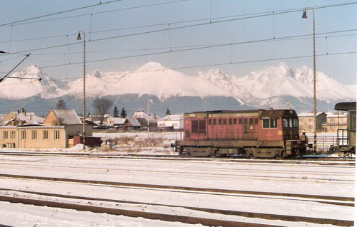  Poprad-Tatry. Motorový rušeň 720 092-6 ?, časť koľajiska stanice, osvetľ. stožiare, trolej. vedenie, vzadu obyt. budovy a zasnežené Tatry. Foto: Z. Piešová, február 1992. 130 x 90, COLOR 