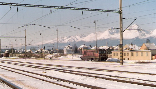 Poprad-Tatry. Motorový rušeň 720 092-6 ?, časť koľaj. stanice, osvetľ. stožiare, trolej. vedenie, vzadu obyt. budovy a zasnežené Tatry. Foto: Z. Piešová, február 1992. 130 x 90, COLOR 