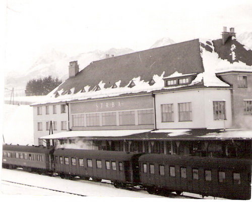  Štrba, zimný pohľad z koľajiska - výpavná budova, za ňou Tatry. V stanici stojí rýchlik (podvozkové vozne, jedna MITROPA). Anon, cca 1950. 88 x 70 