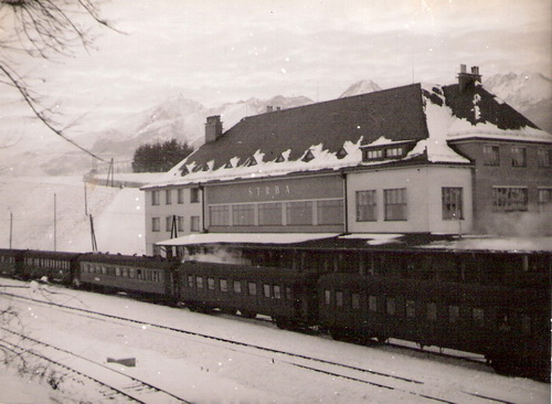  Štrba, zimný pohľad z koľajiska - výpravná budova, za ňou Tatry. V stanici stojí rýchlik (podvozkové vozne, jedna MITROPA). Anon, cca 1950. 118 x 90 