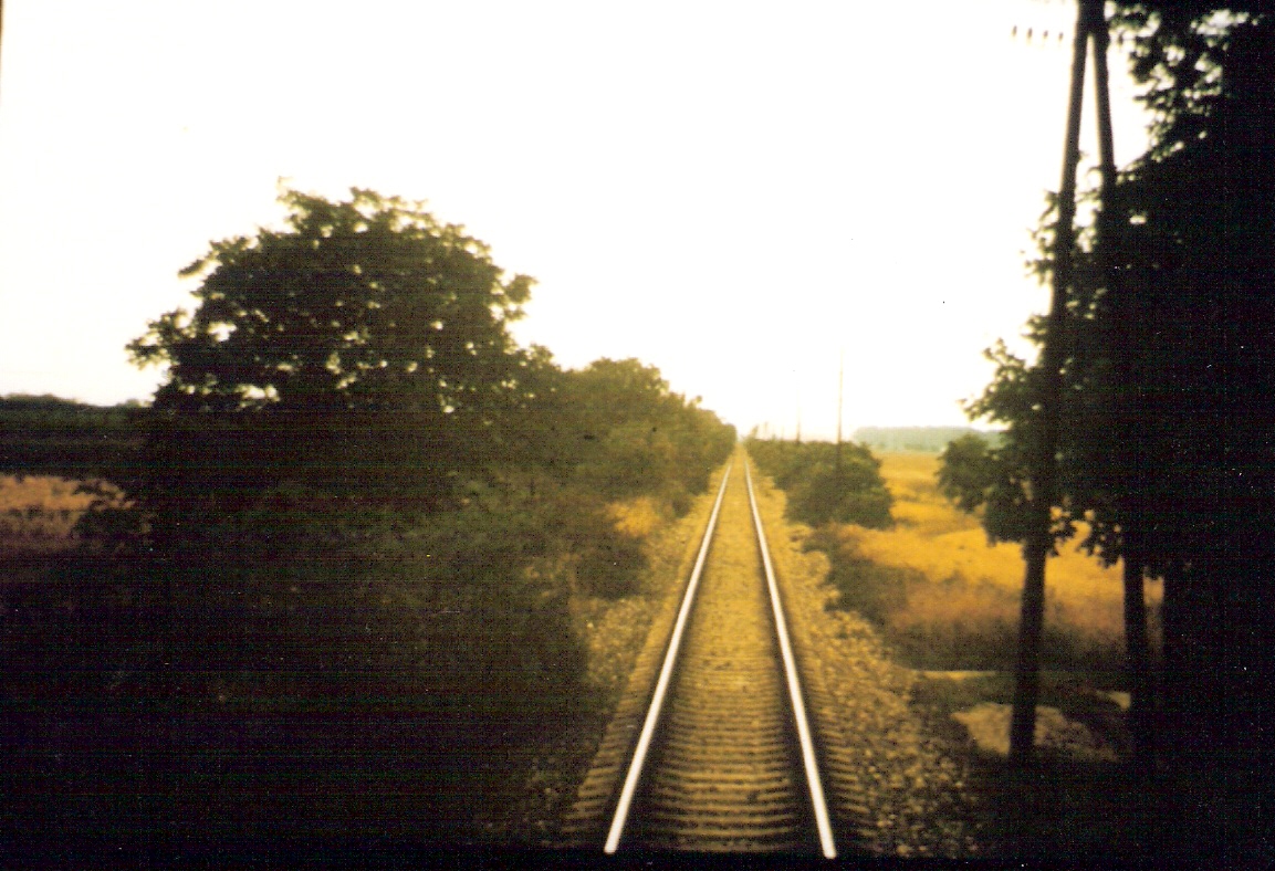  Trať Bratislava-Petržalka - Rusovce. Pohľad zo stred. dverí posled. vozňa na priamy úsek s telegraf. tyčami. Foto: M. Entner, 1990. 150 x 100, COLOR 