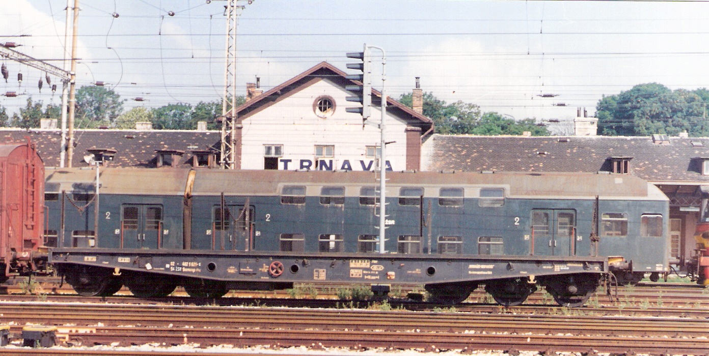  Šesťnápravový plošinový vozeň Sammp/Px. Za ním vozeň poschodovej os. súpravy. Návestidlo AŽD. Vzadu stará výpr. budova Trnava. Foto: M. Entner, 1994. 177 x 125, COLOR 