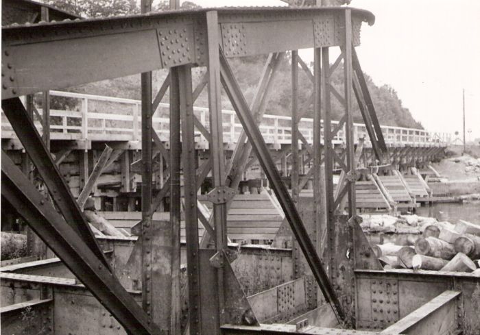  Trosky poloparabolického žel. mosta, vzadu drevené mostné provizórium a stromy, vpravo sklonovník a drevenné kláty . Text: Most cez Hron. Anon., cca 1945. 173 x 122 